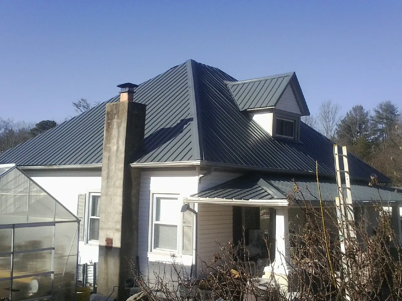 Dark blue standing seam metal roof on a white farmhouse with dormer — Slate & Tile Roof Repair by Roofing Brothers in Odenton