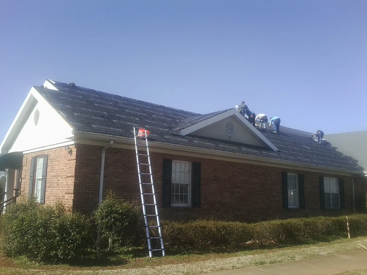 Crew tearing shingles off a brick ranch roof with a ladder set — Emergency Roof Repair work by our crew in Odenton