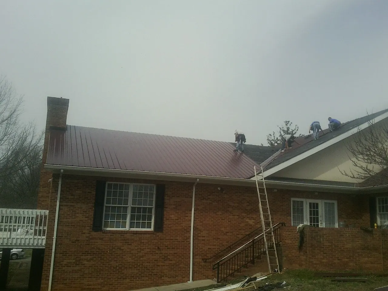 Crew setting red metal roofing panels on a brick home in Odenton