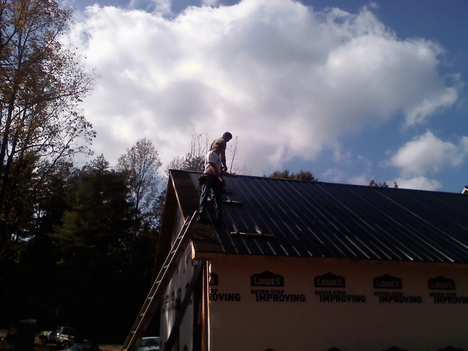 Roofer fastening dark metal panels high against a cloudy sky, from a Roof Inspection job in Odenton