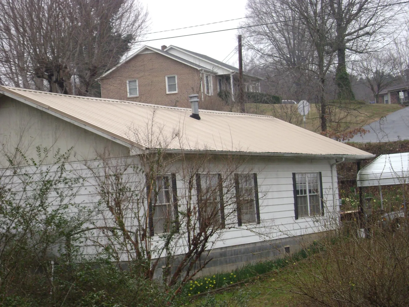 Tan metal roof on a white sided house set into a hillside — Commercial Roofing by Roofing Brothers in Odenton